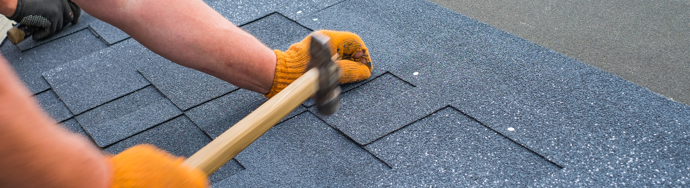 Roofer installing new shingles with a hammer